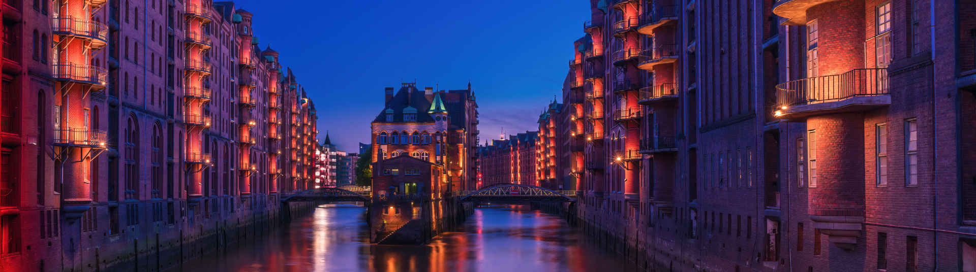 Wasserschloss in der Hamburger Speicherstadt bei Nacht, beleuchtete Backsteingebäude entlang eines Kanals mit Brücken und Spiegelungen im Wasser